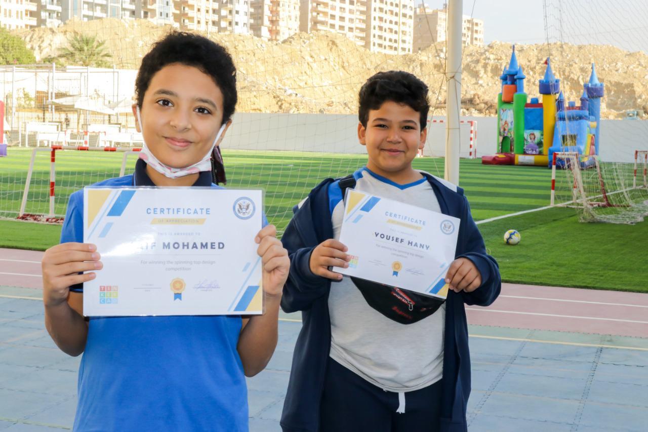 Two boys from IVY STEM International School holding certificates during a sports day event on the school's well-maintained sports field.